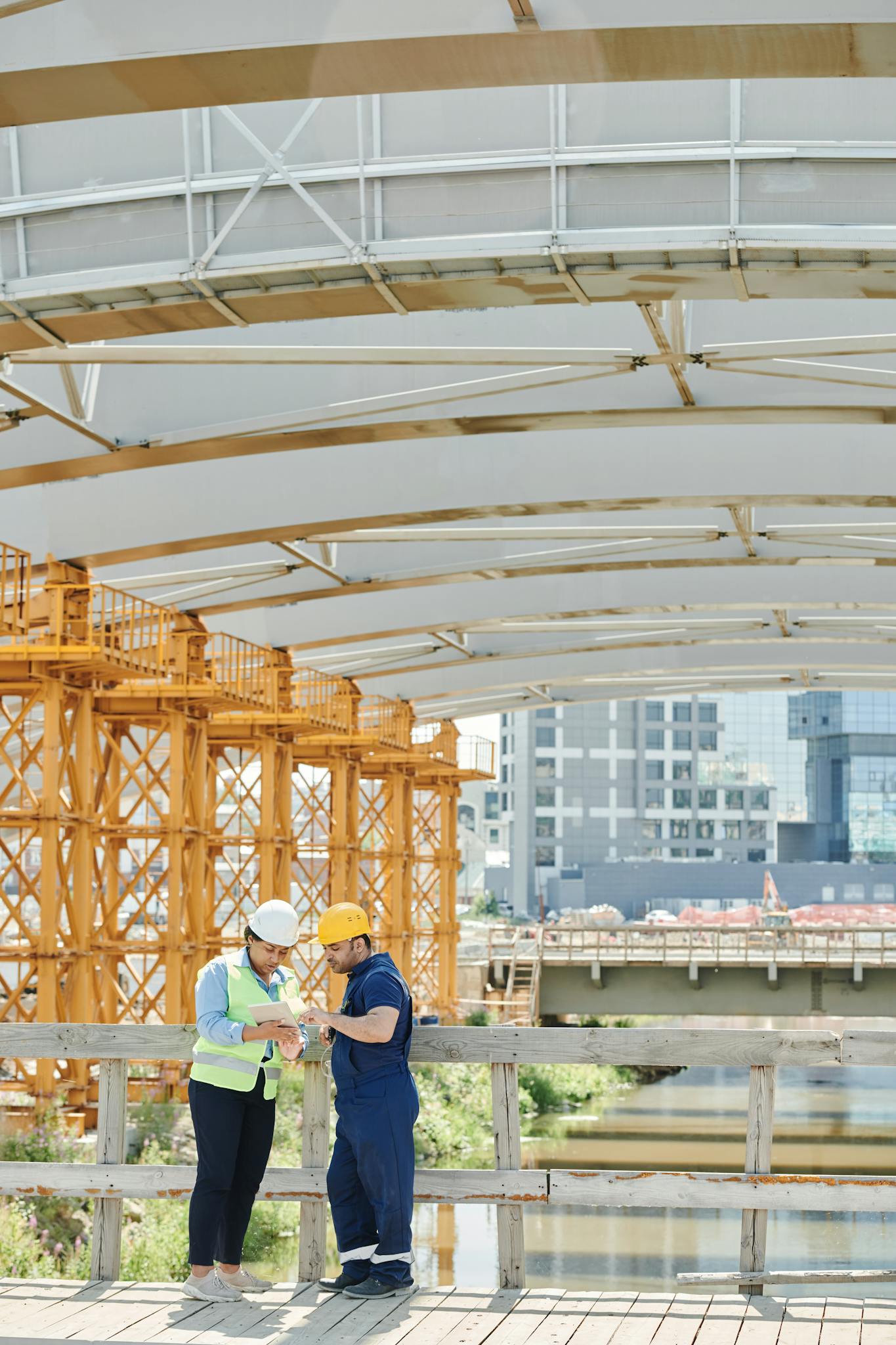 Dois engenheiros discutindo planos em um canteiro de obras ao ar livre sob uma ponte.